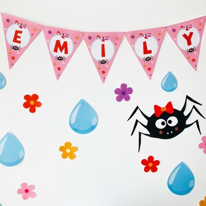 May include: Pink and white banner with the name "EMILY" spelled out in individual flags. Each flag has a black spider with red accents and the words "Tissy Tissy" printed on it. The banner is decorated with blue raindrops, pink, red, and yellow flowers.