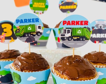 May include: A set of six cupcakes decorated with chocolate frosting and topped with round, colorful cupcake toppers featuring a cartoon garbage truck and the name "Parker".
