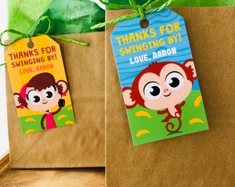 Könnte beinhalten: Zwei braune Papiertüten mit Geschenkanhängern mit Affen- und Mädchenfiguren. Die Anhänger haben einen blauen Hintergrund mit gelben Bananen und dem Text "Danke fürs Vorbeikommen! Liebe, Aaron".
