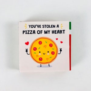 Pu&ograve; includere: Biglietto quadrato con un'illustrazione di pizza a cartoni animati. La pizza ha una faccia sorridente, salame, funghi e peperoni verdi. Il testo recita "YOU'VE STOLEN A PIZZA OF MY HEART".