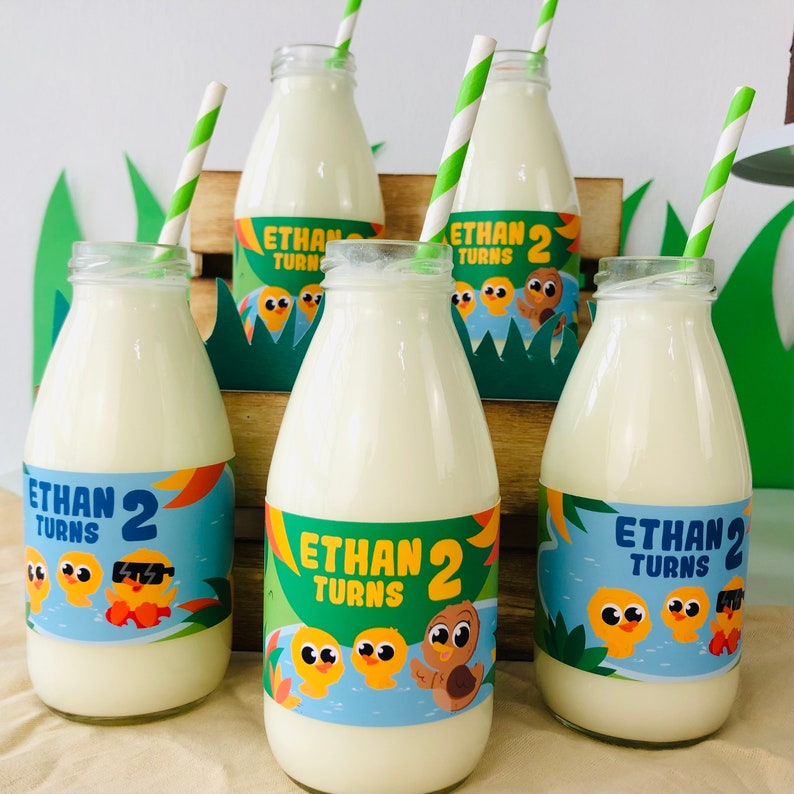 May include: Four glass milk bottles with colorful labels that say "Ethan Turns 2" and feature cartoon ducks. Each bottle has a striped paper straw.