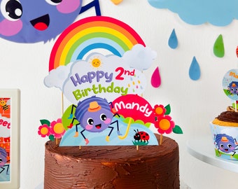 May include: A chocolate cake decorated with a rainbow, a cloud, a spider, and a ladybug. The cake is topped with a sign that says "Happy 2nd Birthday Mandy".