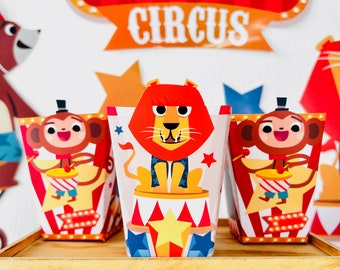 May include: Three colorful party favor boxes with circus animal designs. The boxes feature a lion, a monkey, and a monkey playing a drum. The boxes are decorated with red and white stripes, stars, and a circus tent.