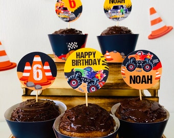 May include: Cupcakes with chocolate frosting and decorative toppers. The toppers feature monster trucks, traffic cones, and the text "Happy Birthday", "Noah", and the number "6". The cupcake liners are navy blue with an orange and white design.