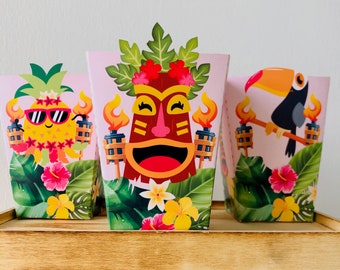 May include: Three pink and white party favor boxes with tropical designs. One box features a pineapple with sunglasses, another features a tiki mask, and the third features a toucan.
