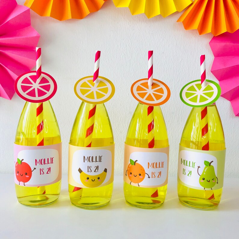 May include: Four clear glass bottles with yellow liquid and red and white striped straws. Each bottle has a colorful fruit sticker with a cute face and the text "Mollie is 2!"