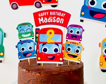 Peut inclure: Un gâteau au chocolat décoré d'une bannière Happy Birthday Madison et de décorations de bus colorés. Les décorations de bus ont des visages souriants et le numéro 2 sur le plus grand bus.