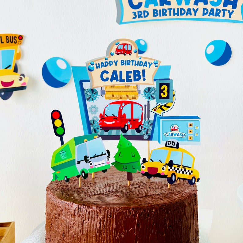 A chocolate cake decorated with a car wash themed cake topper. The topper features a red car, a green trash refuse truck, a yellow taxi, a green tree, and a sign that says "Happy Birthday Caleb!" with the number 3.