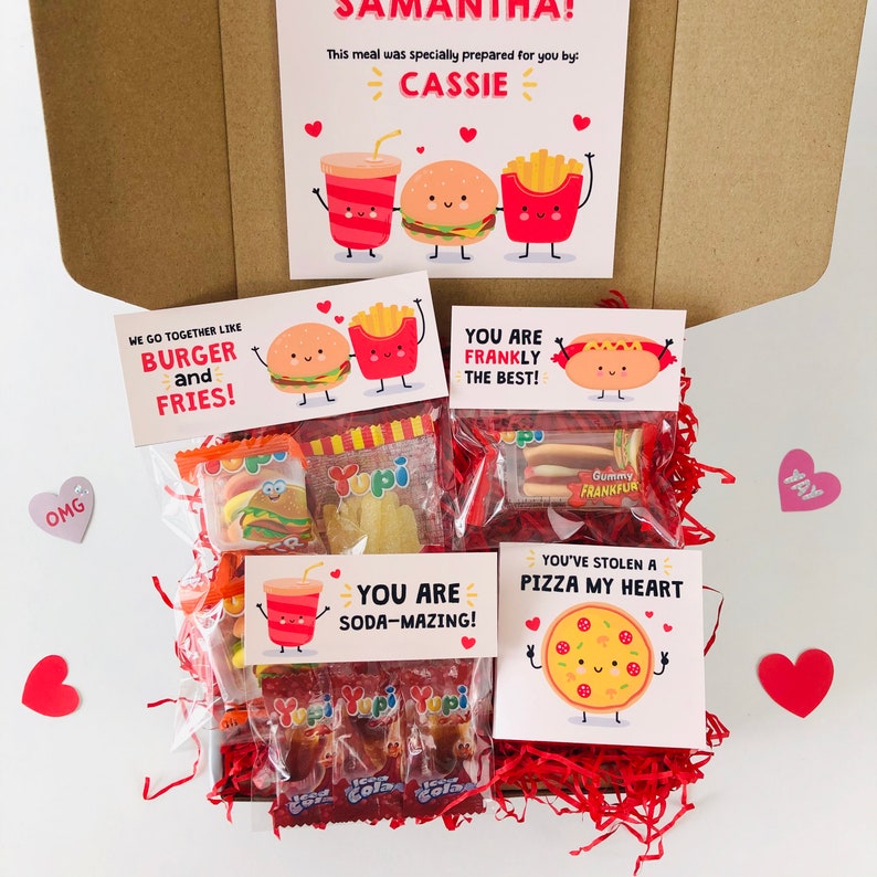 Pu&ograve; includere: Una confezione regalo piena di snack e biglietti. I biglietti presentano illustrazioni di cartoni animati di cibi come hamburger, patatine fritte, pizza e soda. La scatola include caramelle e un messaggio che recita "Samantha! Questo pasto &egrave; stato preparato appositamente per te da: Cassie."