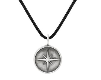 May include: A silver necklace with a black cord and a round pendant featuring a starburst design.