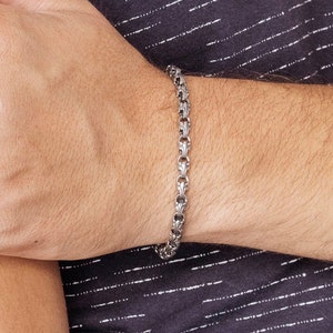 A unique chain bracelet with special beaded links with a hook clasp type closure in oxidized sterling silver that gives it a dark tone and highlights all its details is shown worn by a male model.
