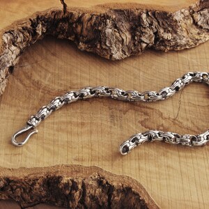 A unique chain bracelet with special beaded links with a hook clasp type closure in oxidized sterling silver that gives it a dark tone and highlights all its details is shown laid down on a wooden surface.