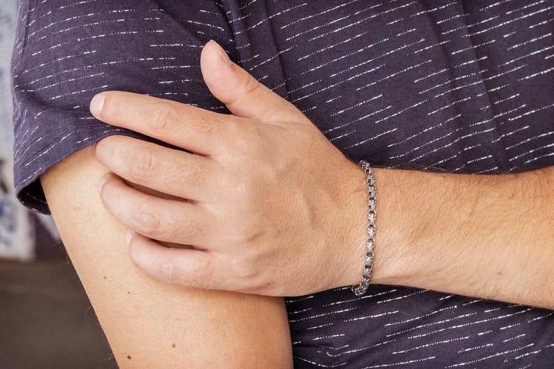 A unique chain bracelet with special beaded links with a hook clasp type closure in oxidized sterling silver that gives it a dark tone and highlights all its details is shown worn by a male model.