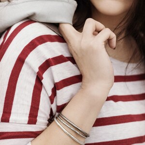 May include: A close-up of a woman's wrist wearing three silver bangles. The woman is wearing a red and white striped shirt.