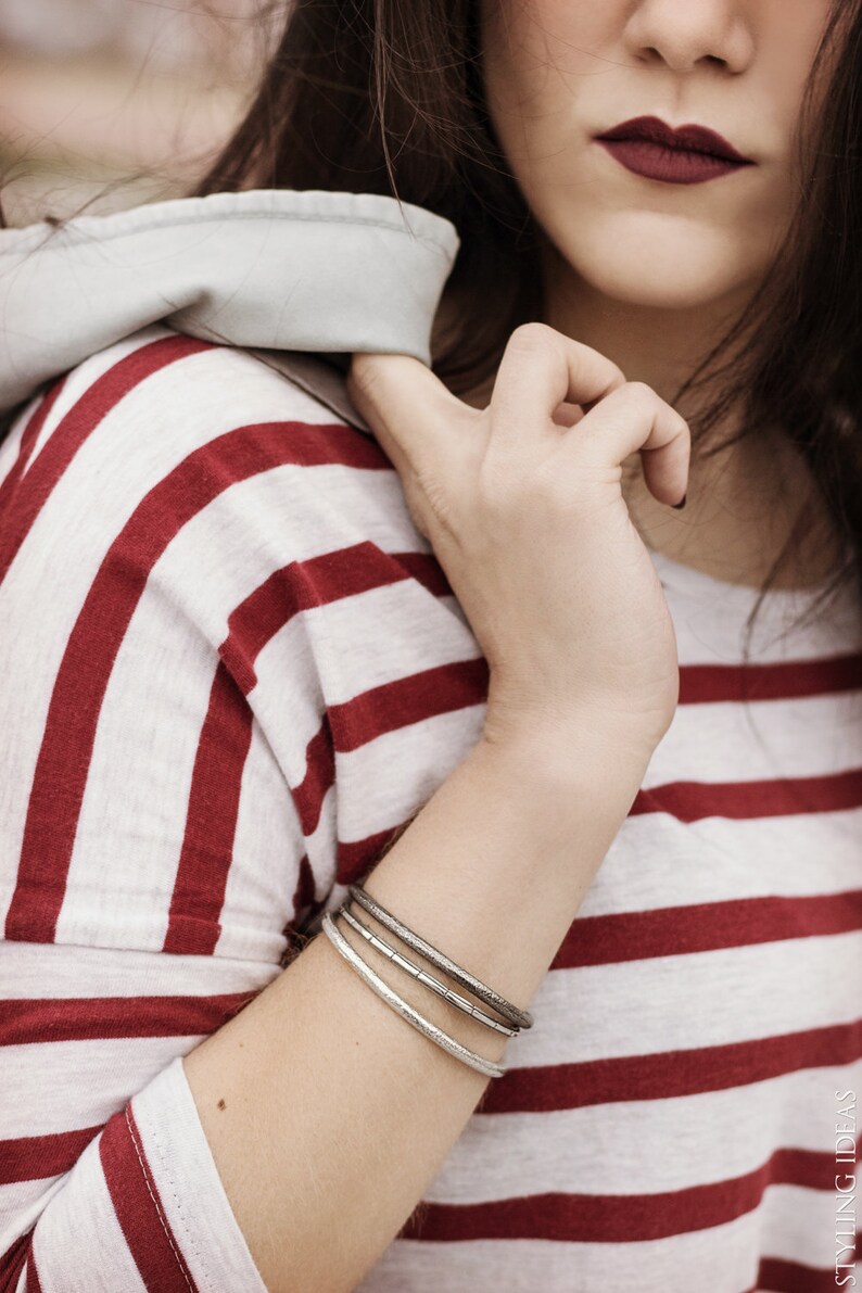 May include: A close-up of a woman's wrist wearing three silver bangles. The woman is wearing a red and white striped shirt.