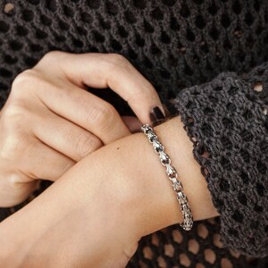 A unique chain bracelet with special beaded links with a hook clasp type closure in oxidized sterling silver that gives it a dark tone and highlights all its details is shown worn by a female model.