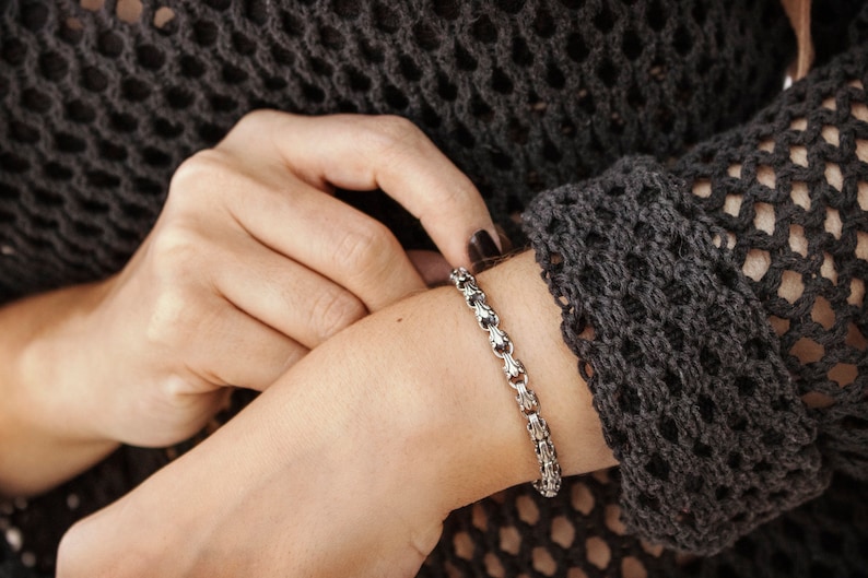 A unique chain bracelet with special beaded links with a hook clasp type closure in oxidized sterling silver that gives it a dark tone and highlights all its details is shown worn by a female model.