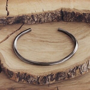 May include: A simple, silver-toned metal bangle bracelet. The bracelet is smooth and has a slightly curved shape.