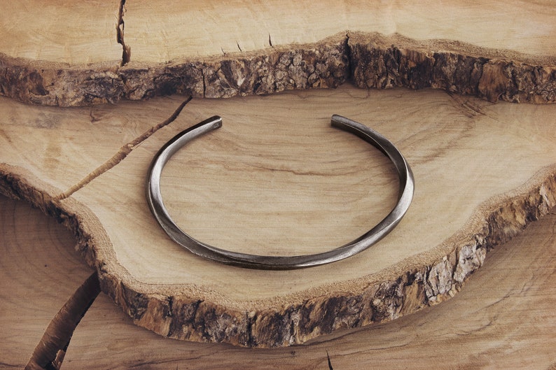May include: A simple, silver-toned metal bangle bracelet. The bracelet is smooth and has a slightly curved shape.