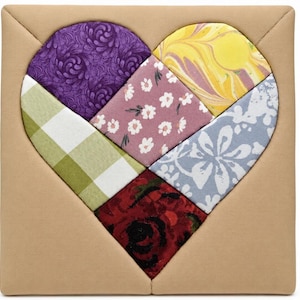 May include: A quilted heart design with various fabric patterns. The heart is composed of sections in purple, pink, yellow, blue, green, and red. The heart shape is set against a tan square background.