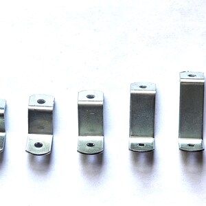 May include: Five silver-colored metal brackets of varying sizes are arranged in a row. Each bracket has a U-shape with a hole on the top and bottom. The brackets are made of a shiny, reflective metal.
