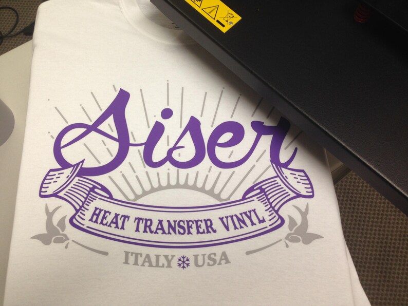 K&ouml;nnte beinhalten: Ein wei&szlig;es T-Shirt mit einem violetten Design, auf dem "Siser Heat Transfer Vinyl Italy USA" mit einem Schneeflocken-Symbol steht.