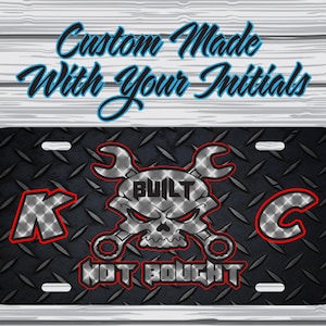 May include: Black and silver license plate with a skull and crossed wrenches. The text "BUILT NOT BOUGHT" is below the skull. The letters "K" and "C" are on either side of the skull.
