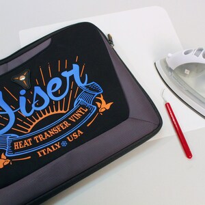 K&ouml;nnte beinhalten: Eine schwarze Laptoptasche mit einem wei&szlig;en Logo, auf dem "Siser Heat Transfer Vinyl Italy USA" mit einer Sonne und V&ouml;geln steht. Auf dem Bild sind auch ein wei&szlig;es B&uuml;gelbrett mit einem wei&szlig;en B&uuml;geleisen und ein rotes Unkrautentfernungswerkzeug zu sehen.