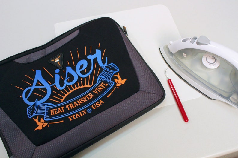 K&ouml;nnte beinhalten: Eine schwarze Laptoptasche mit einem wei&szlig;en Logo, auf dem "Siser Heat Transfer Vinyl Italy USA" mit einer Sonne und V&ouml;geln steht. Auf dem Bild sind auch ein wei&szlig;es B&uuml;gelbrett mit einem wei&szlig;en B&uuml;geleisen und ein rotes Unkrautentfernungswerkzeug zu sehen.