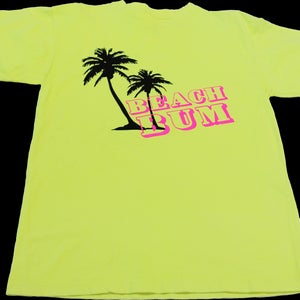 K&ouml;nnte beinhalten: Ein neongelbes T-Shirt mit einer schwarzen Silhouette von zwei Palmen und dem Text "BEACH BUM" in rosa Buchstaben.