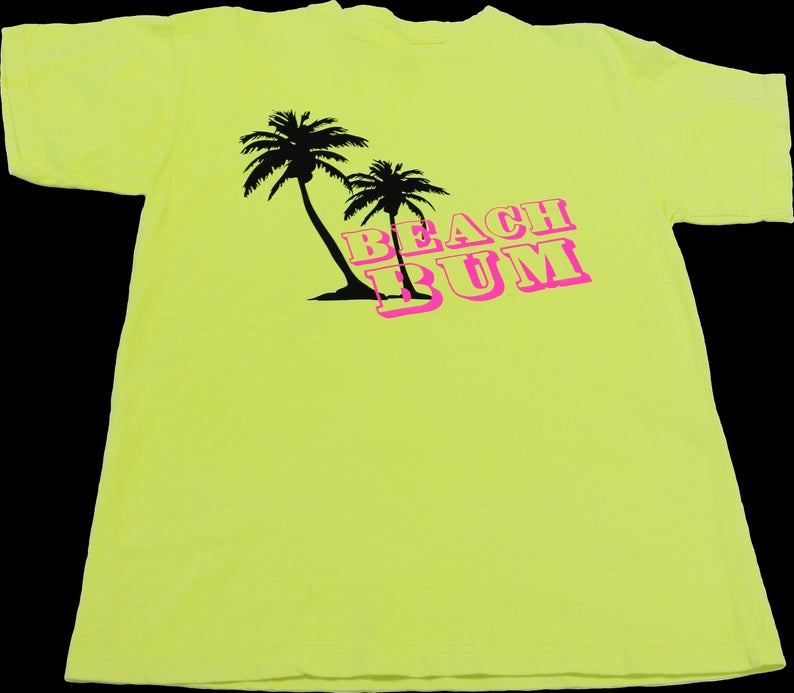 K&ouml;nnte beinhalten: Ein neongelbes T-Shirt mit einer schwarzen Silhouette von zwei Palmen und dem Text "BEACH BUM" in rosa Buchstaben.