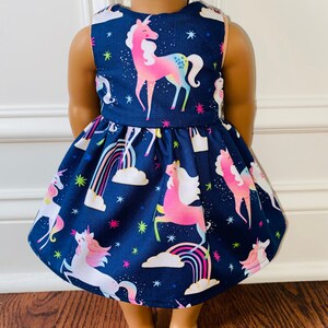May include: A navy blue dress with a unicorn print. The dress features a white and pink unicorn with a rainbow and clouds. The dress is sleeveless and has a gathered skirt.