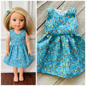 May include: A doll wearing a sleeveless blue dress patterned with colorful Christmas lights. The dress has a round neckline and a gathered skirt. The doll has blonde hair and blue eyes. A matching hair clip is visible.