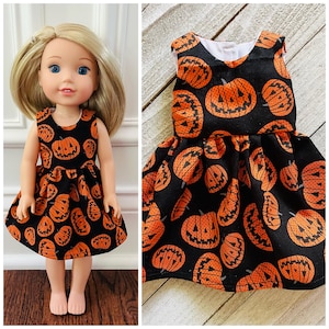 May include: A sleeveless black doll dress with an orange jack-o'-lantern pattern. The dress has a round neckline and a flared skirt. The doll has blonde hair and blue eyes. The dress is designed for a doll.