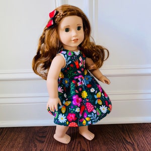 May include: A doll wearing a green dress with a floral print featuring butterflies, flowers, and mushrooms. The dress has a red bow in the hair.