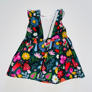 May include: A green dress with a white bodice and a floral print featuring mushrooms, butterflies, and flowers. The dress has a gathered skirt and a V-neckline.