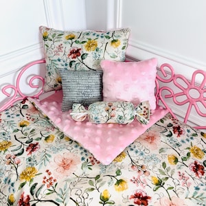 May include: A pink metal bed frame with floral patterned bedding and pillows. The bedding includes a floral patterned blanket, a pink dotted blanket, and several pillows in various sizes and patterns. A decorative candy-shaped pillow is also present.
