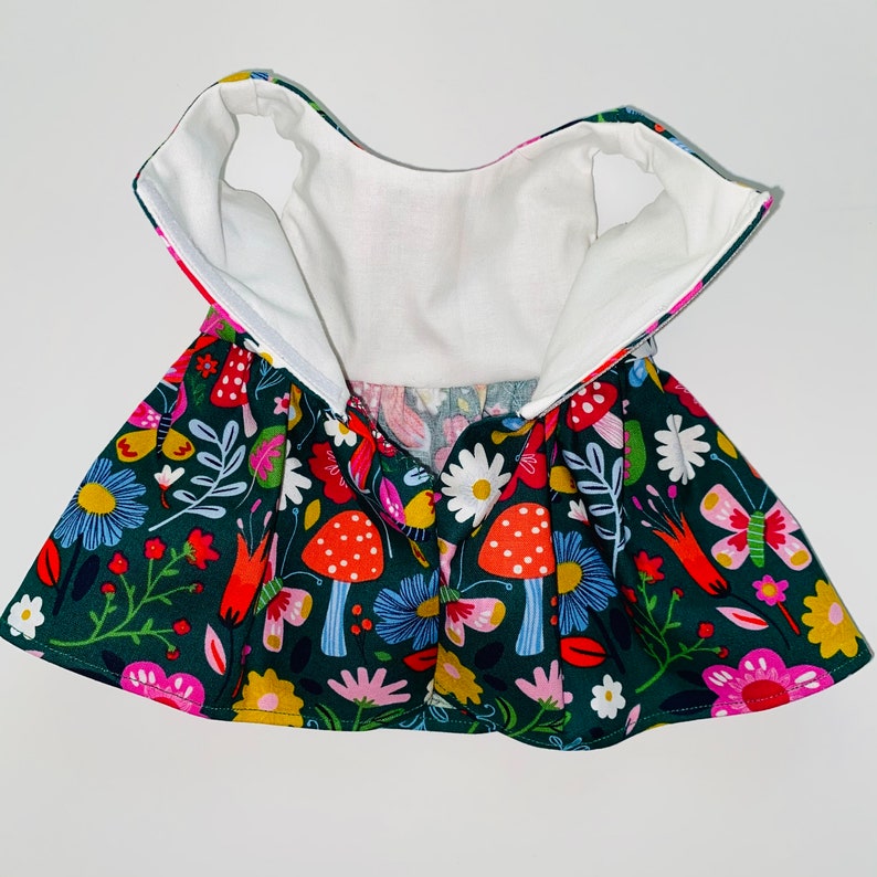 May include: A green dress with a white lining and a colorful floral print featuring mushrooms, butterflies, and flowers.