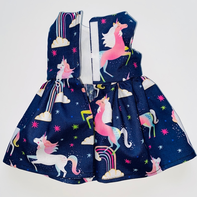 May include: A dark blue dress with a unicorn print. The dress has a white zip down the back and features rainbows, stars, and clouds.