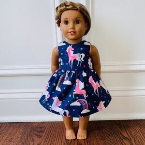 May include: A blue dress with a unicorn and rainbow print for a doll. The dress has a sleeveless bodice and a full skirt.