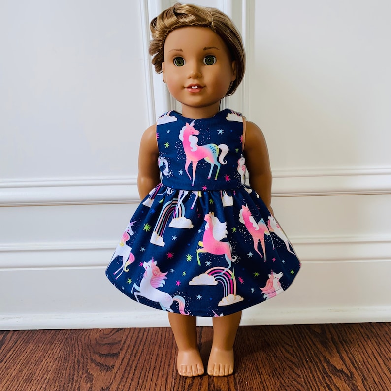 May include: A blue dress with a unicorn and rainbow print for a doll. The dress has a sleeveless bodice and a full skirt.