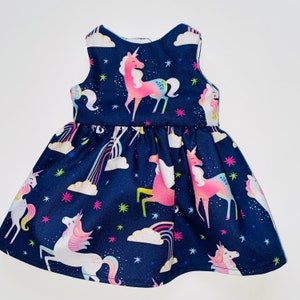May include: A navy blue sleeveless dress with a unicorn print. The dress features a variety of colourful unicorns with rainbows and stars on a dark blue background.