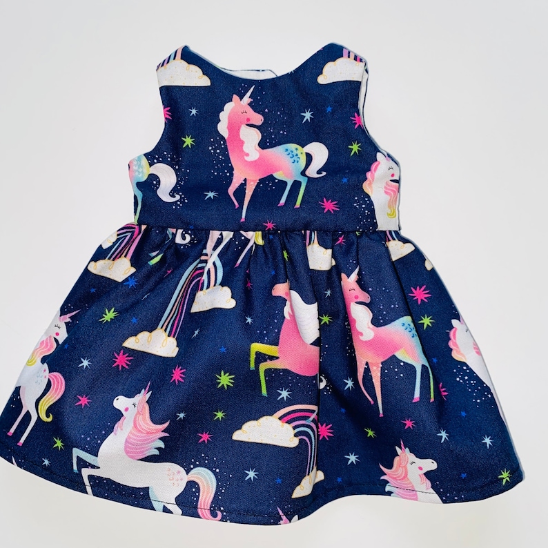 May include: A navy blue sleeveless dress with a unicorn print. The dress features a variety of colourful unicorns with rainbows and stars on a dark blue background.