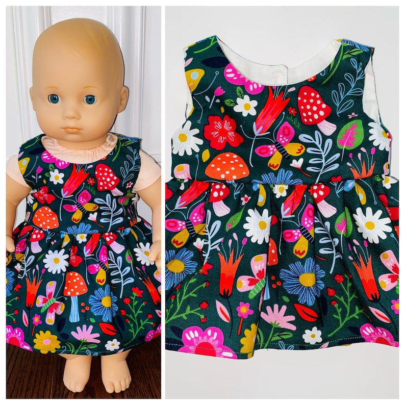 May include: A green dress with a floral print featuring butterflies, mushrooms, and flowers. The dress has a white bodice and is sleeveless.