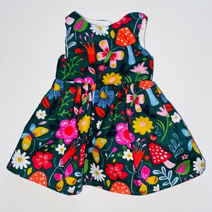 May include: A green sleeveless dress with a colorful floral and butterfly print. The dress has a gathered skirt and a fitted bodice.