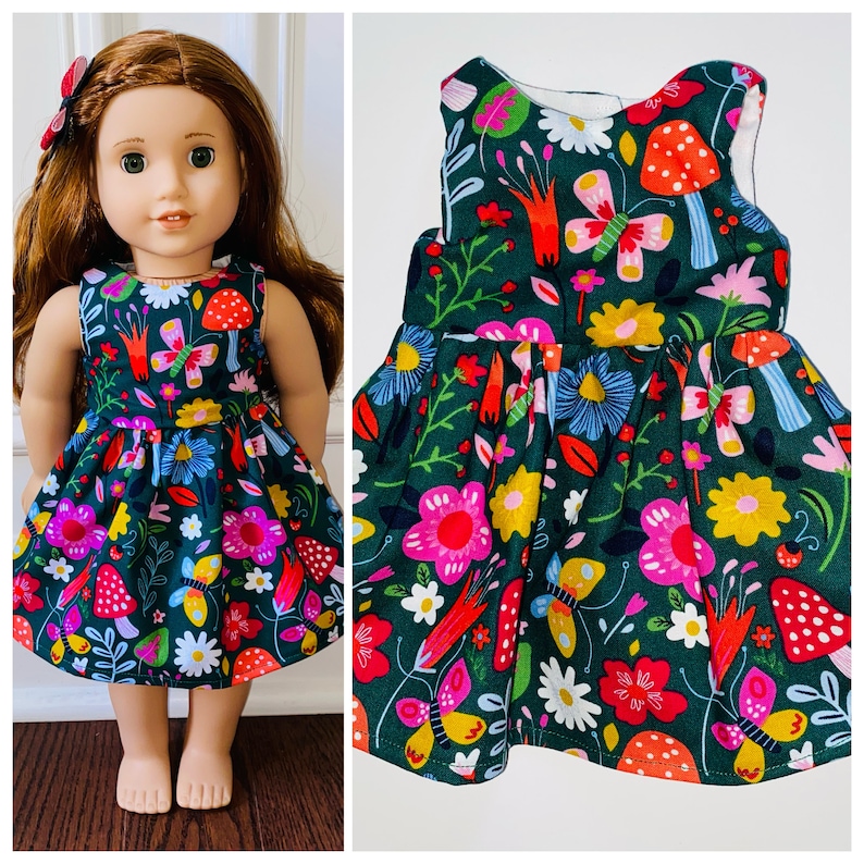May include: A green sleeveless dress with a floral print featuring butterflies, mushrooms, and flowers. The dress has a gathered skirt and is perfect for a doll.
