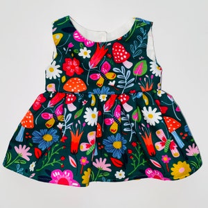 May include: A green sleeveless dress with a colorful floral and mushroom print. The dress has a gathered skirt and a white neckline.