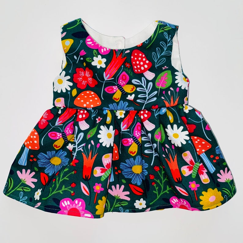 May include: A green sleeveless dress with a colorful floral and mushroom print. The dress has a gathered skirt and a white neckline.