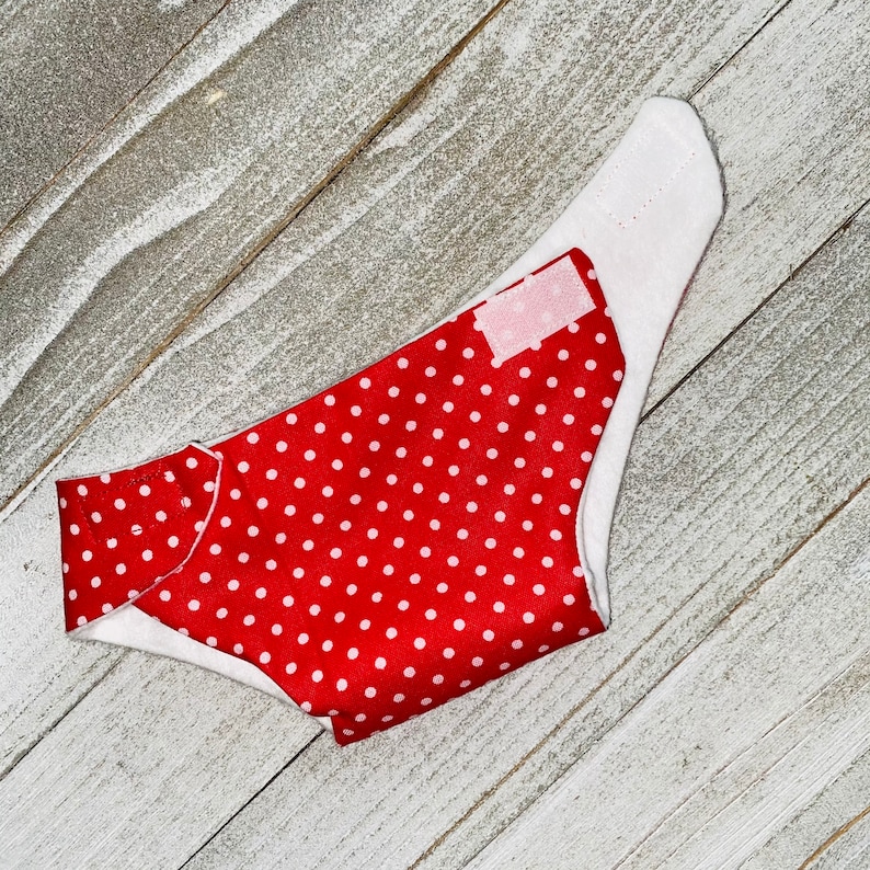 May include: Red and white polka dot fabric with a white trim. The fabric is folded in half and has a white label on the front.