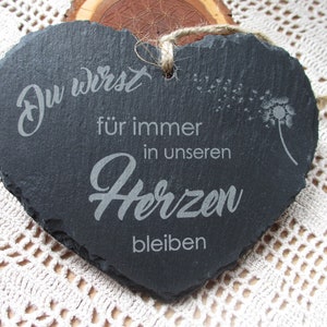 K&ouml;nnte beinhalten: Eine schwarze, herzf&ouml;rmige Schiefertafel mit dem Text "Du wirst f&uuml;r immer in unseren Herzen bleiben" und einem L&ouml;wenzahnmuster.
